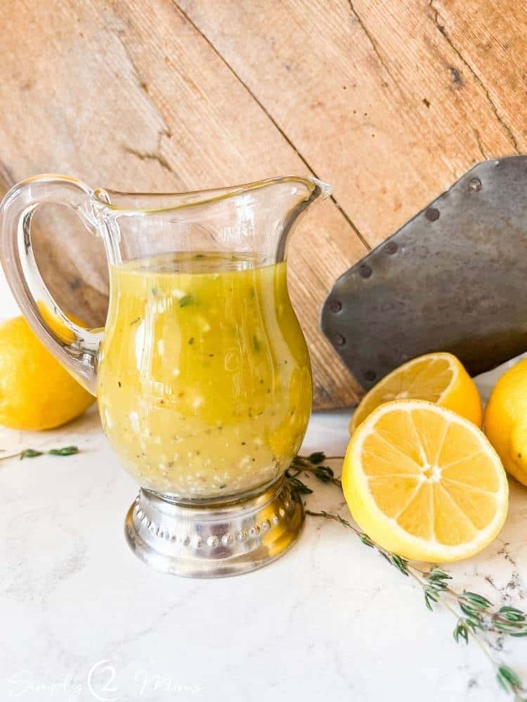 Small glass pitcher filled with sweet lemon vinaigrette dressing with fresh lemons.