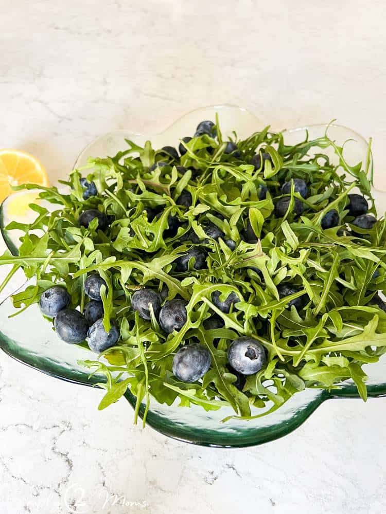Green glass salad bowl filled with baby arugula and large fresh blueberries.