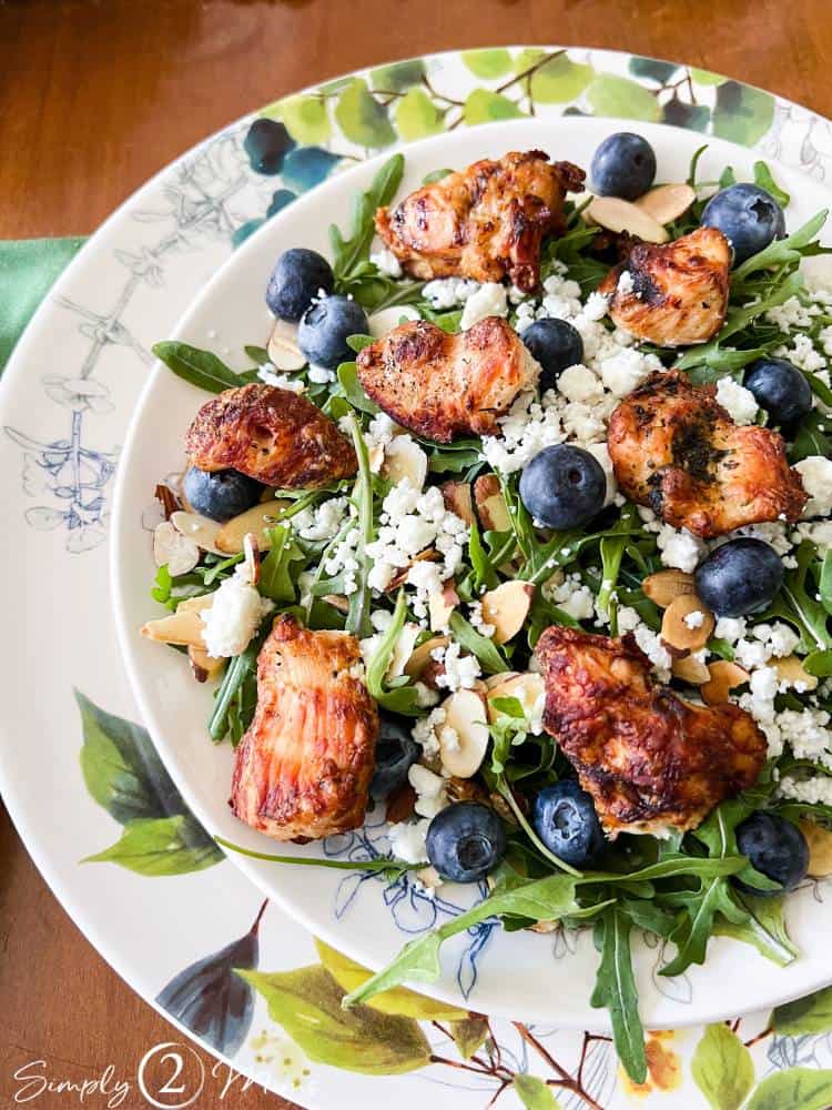 Plate of entre arugula salad with fresh blueberries, toasted almonds, goat cheese, and grilled chicken.