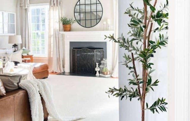 7 foot faux olive tree in a large basket by a white built in in a neutral family room decorated for spring and summer.