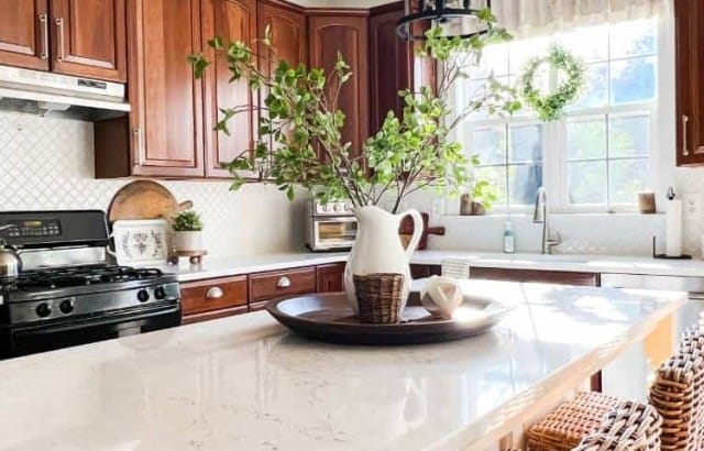 Kitchen with cherry cabinets, painted island, and quartz counters decorated for spring with greenery and white accents.