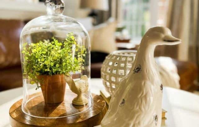 Round white coffee table decorated for spring with a glass bell jar displaying a potted plant and white bird.