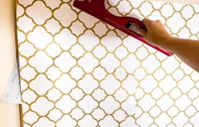 Hand using a straight-edge smoothing tool to install peel-and-stick wallpaper.