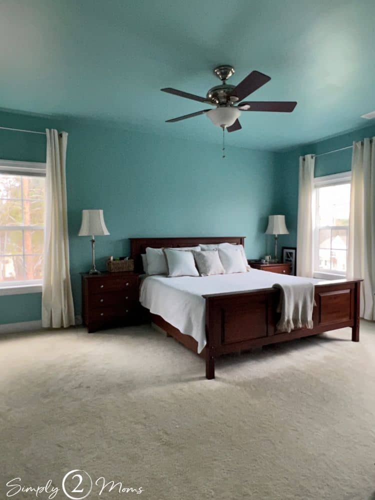 Main bedroom with turquoise ceiling and walls, cherry bed with white bedding, white curtains, and ceiling fan.