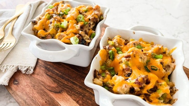 Two square baking ramekins with handles filled with low carb bacon hot chicken salad topped with melted cheddar cheese.