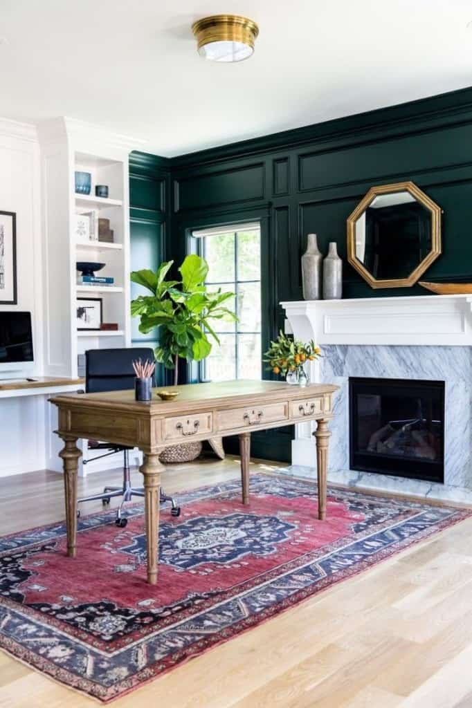 Inspiration photo of an office with dark green walls with picture frame boxes, fireplace, red oriental rug, and desk.