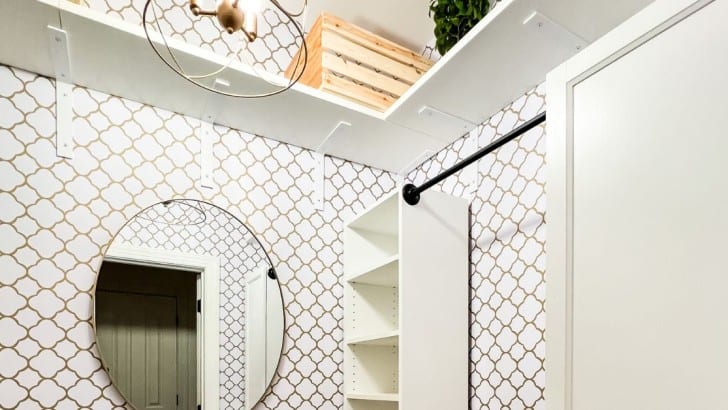 Small wallpapered square walk-in closet with IKEA Billy bookcase with added shelves and hanging rod attached.