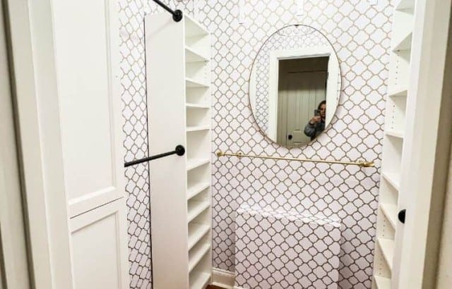 Small square walk-in closet with IKEA Billy shelves, hanging rods, upper storage shelf, and rod to hang jeans with S hooks.