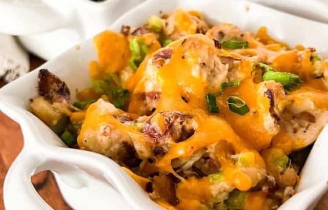 Southern hot chicken salad with bacon topped with melted cheddar cheese and sliced green onions in individual square baking dishes.