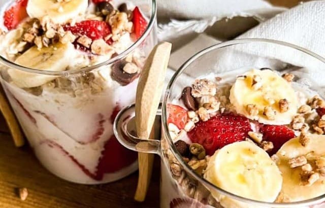 Two glass containers with wood spoons filled with healthy strawberry banana overnight oats topped with granola.