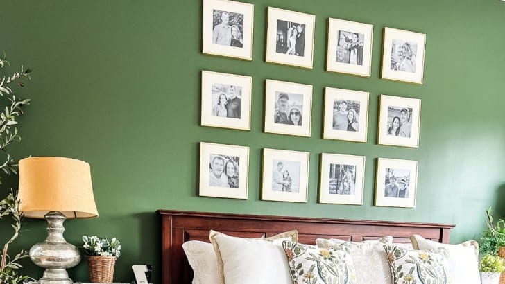 Dark green wall above a king size cherry headboard with 12 black and white photos with white mats and gold frames.