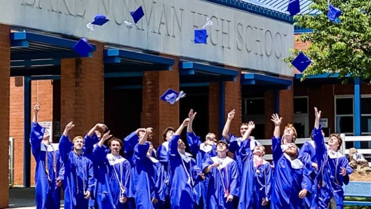 group of boys in graduation gowns tossing caps in front of high school feature