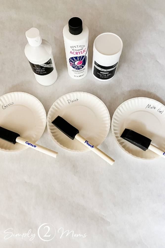 Paper plates labeled with "gesso," "paint," and "matte gel" and foam brushes on the plates.
