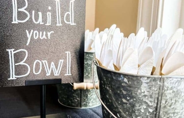 chalkboard on table next to plastic utensils in galvanized bucket