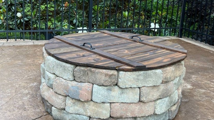 completed wood cover with handles on top of DIY stone firepit on patio