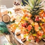 Table spread for a tropical cocktail party with assorted appetizers and a pineapple with skewers .