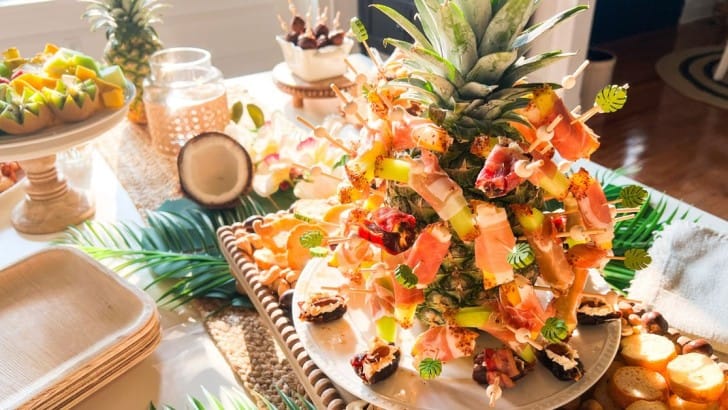 Table spread for a tropical cocktail party with assorted appetizers and a pineapple with skewers .