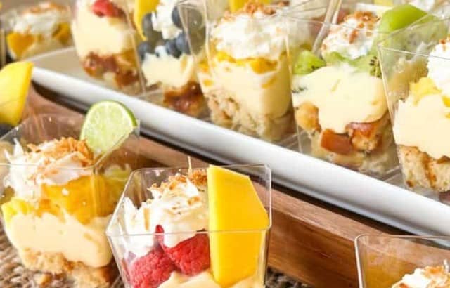 Mini plastic cups of keto tropical trifle parfaits with a variety of diced fruit on a white platter.