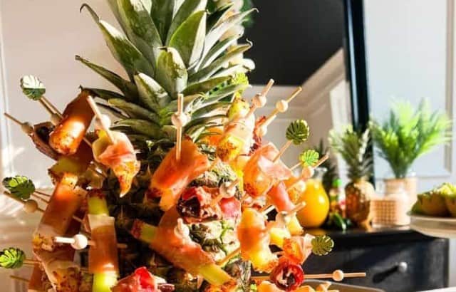 Fresh pineapple as a centerpiece on a cocktail party table displaying assorted appetizers on cocktail picks.