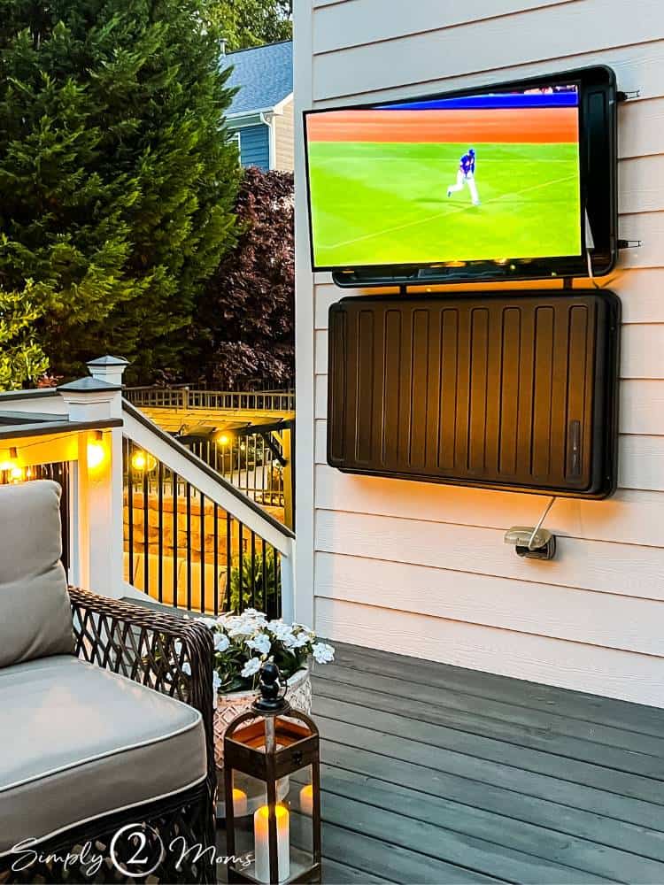 TV in hard plastic cover hanging on siding of house on deck