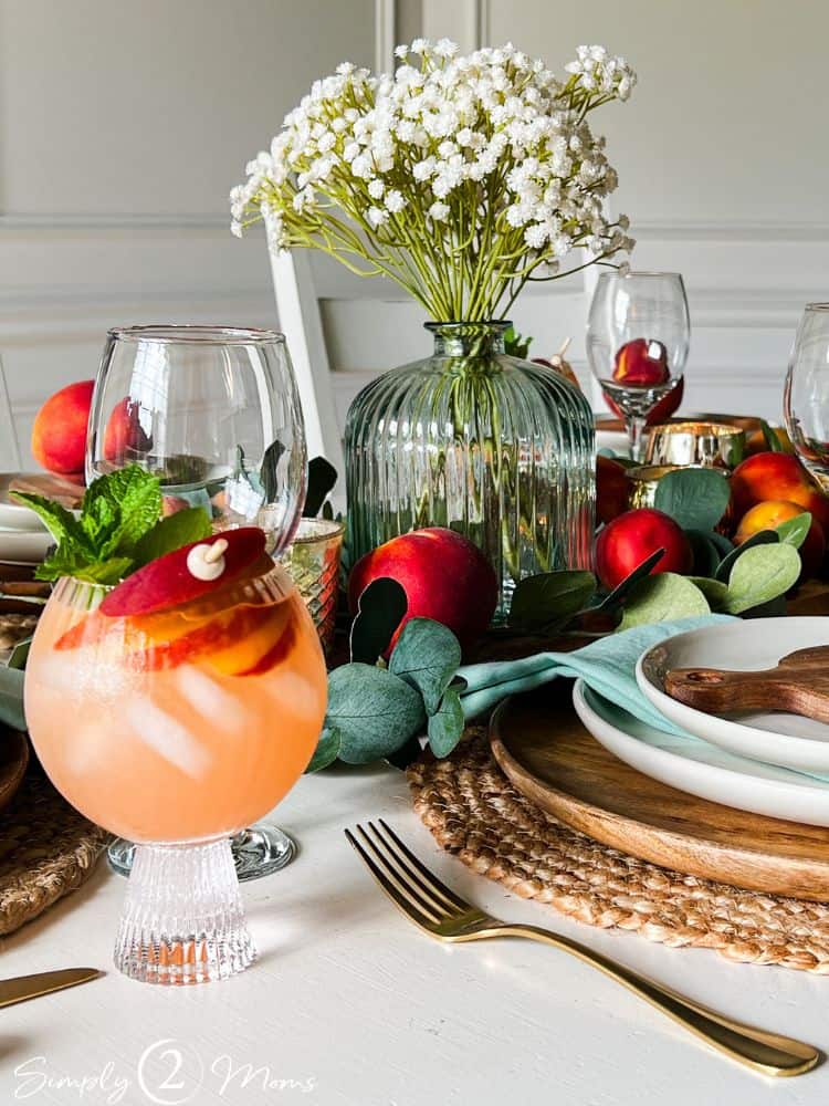 Table decorated for a peach-themed dinner party with a goblet of peach sangria garnished with peach slices.