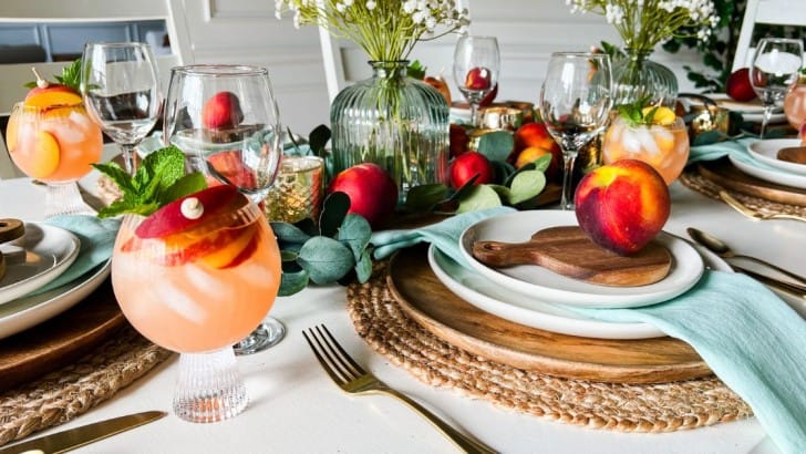 Table decorated for a peach-themed dinner party with goblets of peach sangria at each place setting.