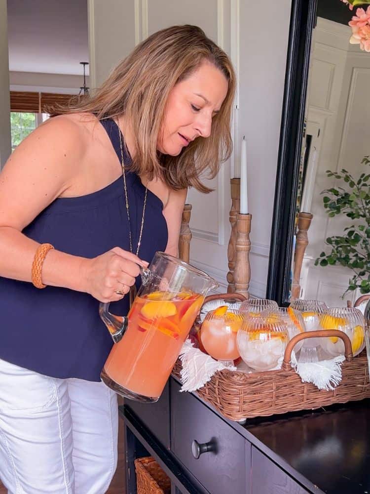 Woman pouring peach sangria into goblets at a dinner party.