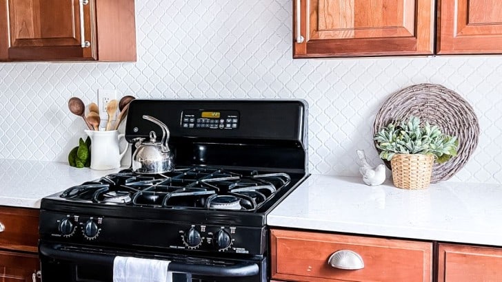 Matte white lantern tiles installed as a kitchen backsplash with white grout in a kitchen with light cherry cabinets..