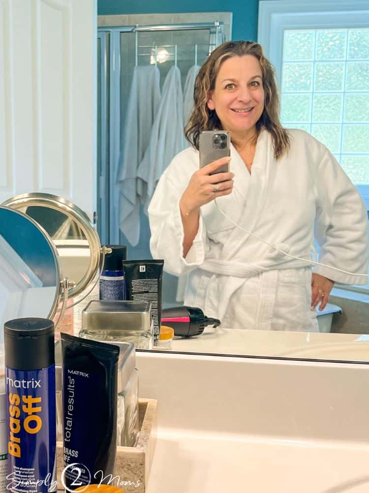 Woman with wet and wavy highlighted ash brown hair standing in a bathroom before drying it.