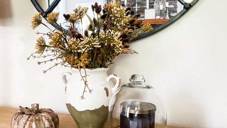 White Tuscan pottery urn filled with a variety of faux fall stems on a console tab.e