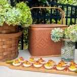 Table with picnic basket and basket of hydrangeas with a wood serving board of deviled eggs for a Southern Potluck Dinner.