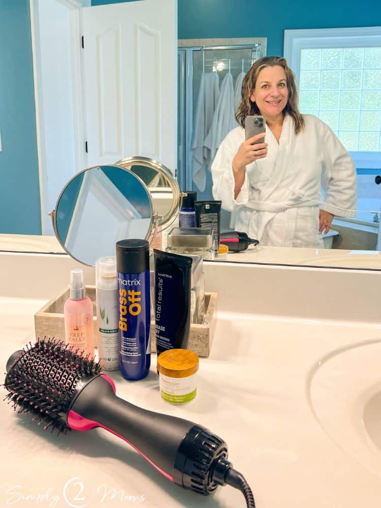 Woman with wet hair in a bathroom with hair care favorites on the bathroom counter.