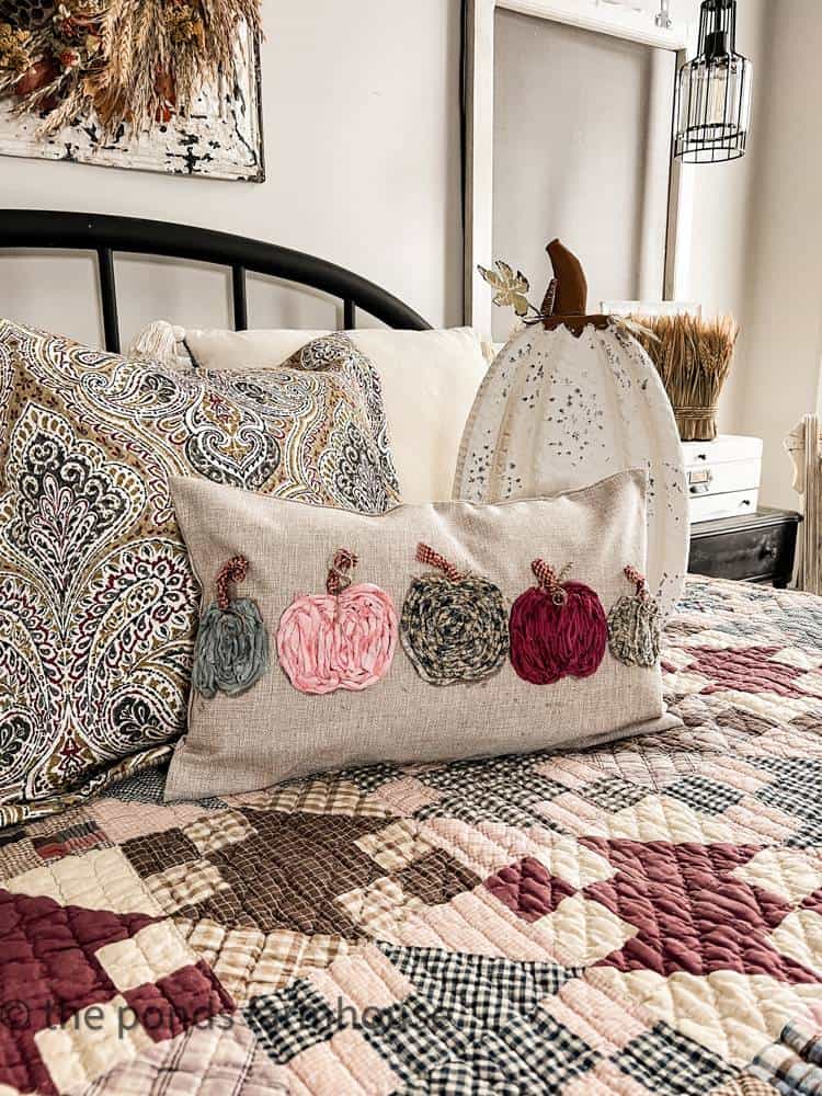 knit pumpkins across front of neutral pillow on bed with quilt
