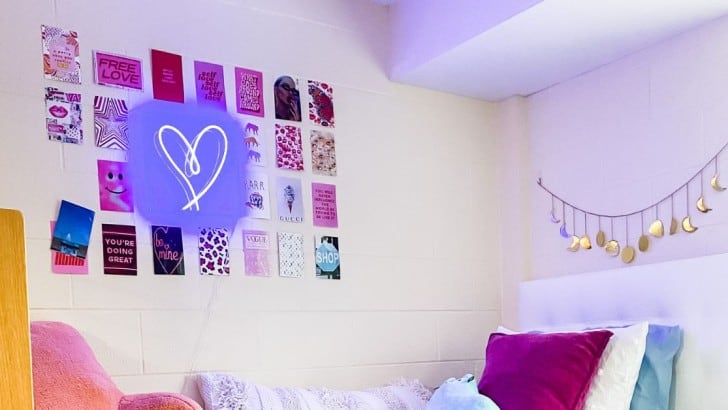 Dorm room wall with photo collage cards and neon heart hanging over the bed.