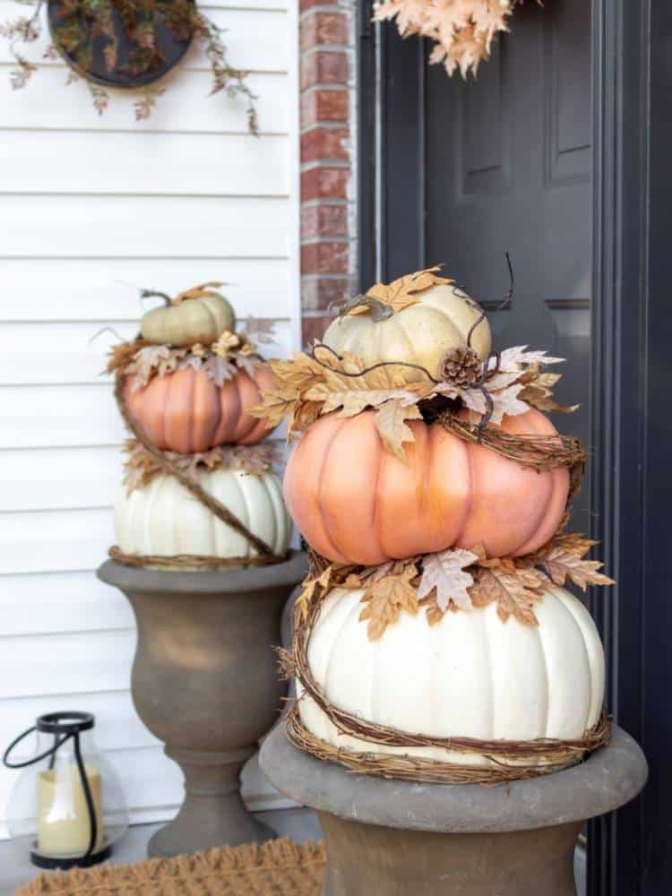 stacked pumpkins in urn style planters by front door