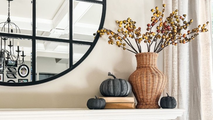 Woven vase with fall stems on a fireplace mantel with vintage books and upcycled black faux pumpkins.