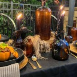 Outdoor table decorated with amber bottles and Halloween decor. Mini pumpkins filled with chili are on each dinner plate.