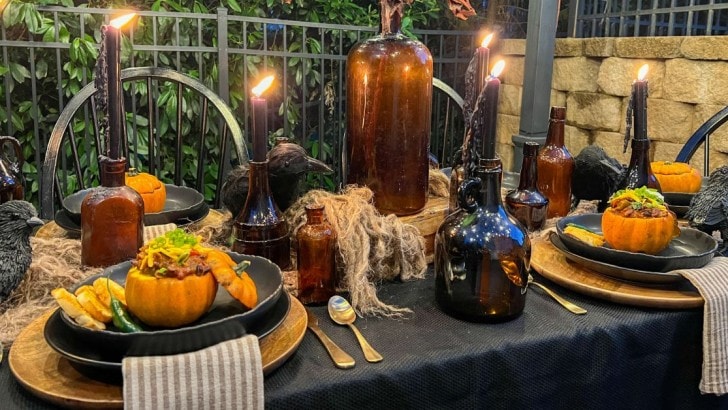 Outdoor table decorated with amber bottles and Halloween decor. Mini pumpkins filled with chili are on each dinner plate.