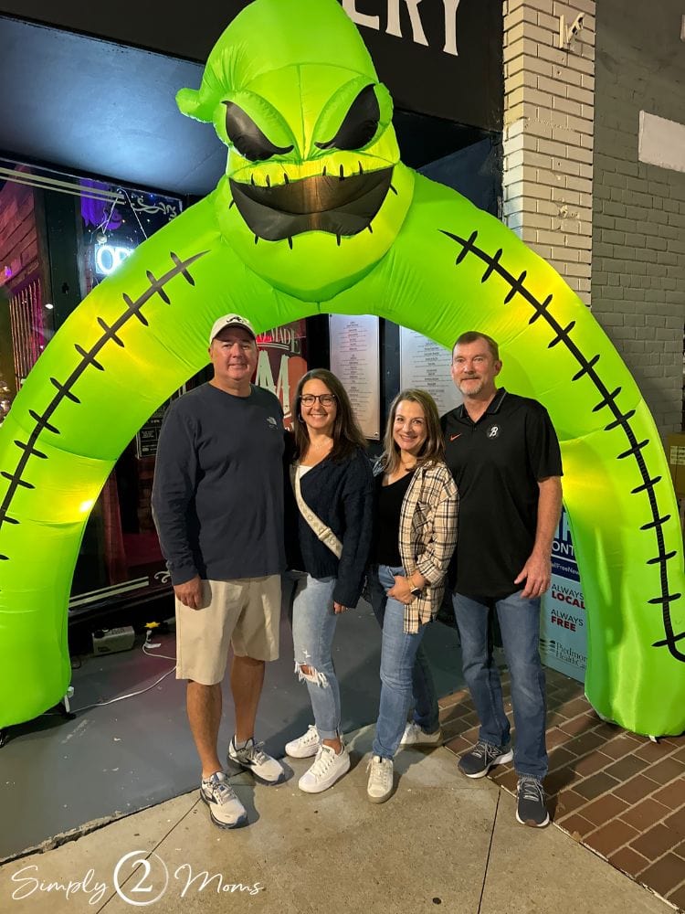 Two couples standing under a Halloween inflatable.
