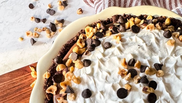 White scalloped pie plate of keto Chocolate Hazelnut pie garnished with hazelnuts and sugar free chocolate chips.