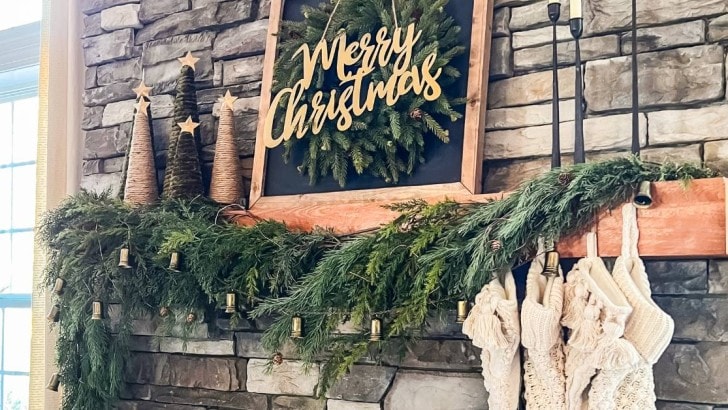 stone fireplace with wood mantel decorated for Christmas with greenery and knit stockings