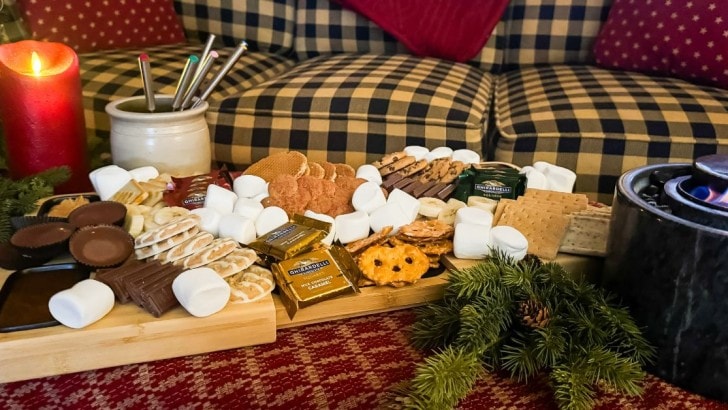 Wood charcuterie board filled with cookies, candy, and marshmallows next to a mini indoor firepit for Christmas s'mores.