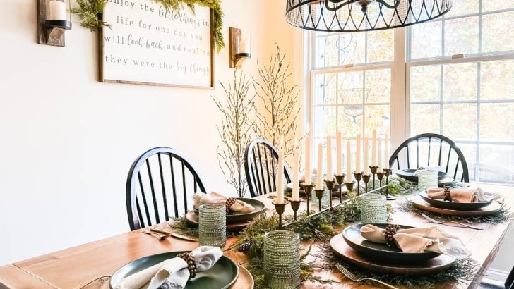 wood table with black wood chairs set with greenery for holidays windows behind table