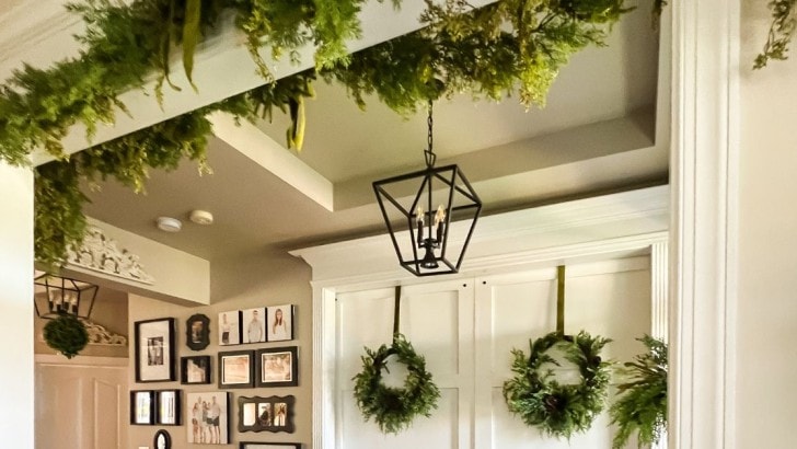 Foyer of a traditional style home with greenery wreaths hanging on sliding doors and greenery garland above the door ways.
