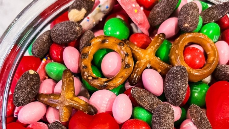 Pretzels shaped like x's and o's lined up to spell xoxo in a Valentine's snack mix with chocolate almonds and candies.