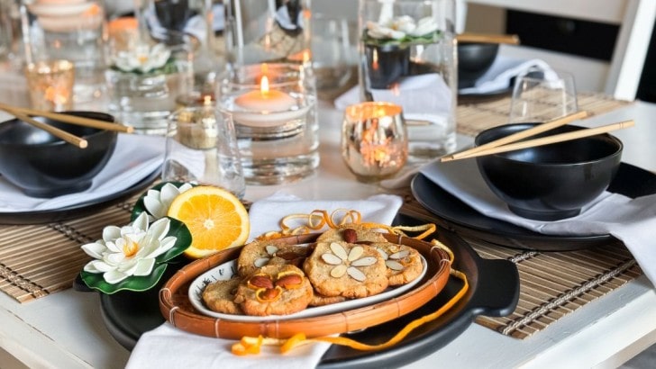 Plate of almond cookies garnished with oranges and lotus blossoms on a table set for an Asian dinner party.