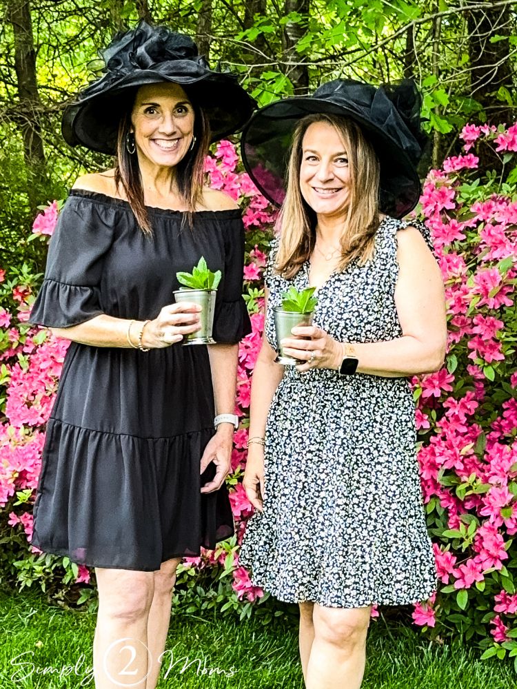 AnnMarie and Anne from Simply2Moms wearing fancy black hats and holding silver julep cups for a Derby Day party.