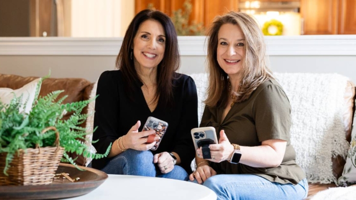 two women sitting on couch holding iphones