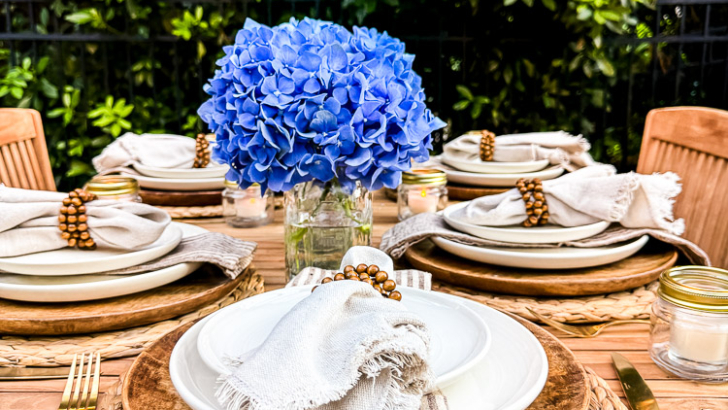 neutral place setting on wood outdoor table with greenery beyond space