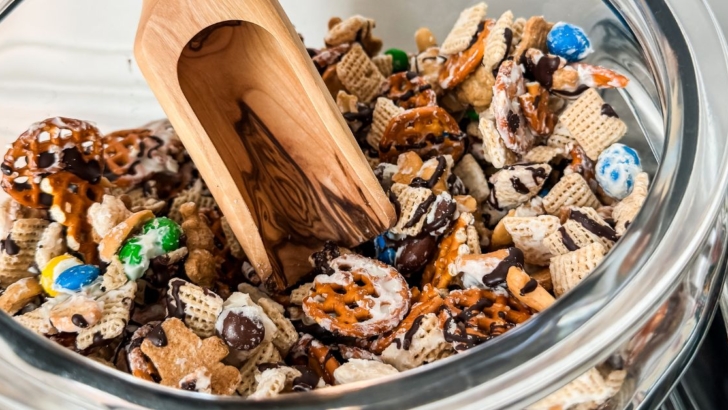 Sweet and salty snack mix coated in white chocolate and drizzled with dark chocolate in a jar with wood scoop.
